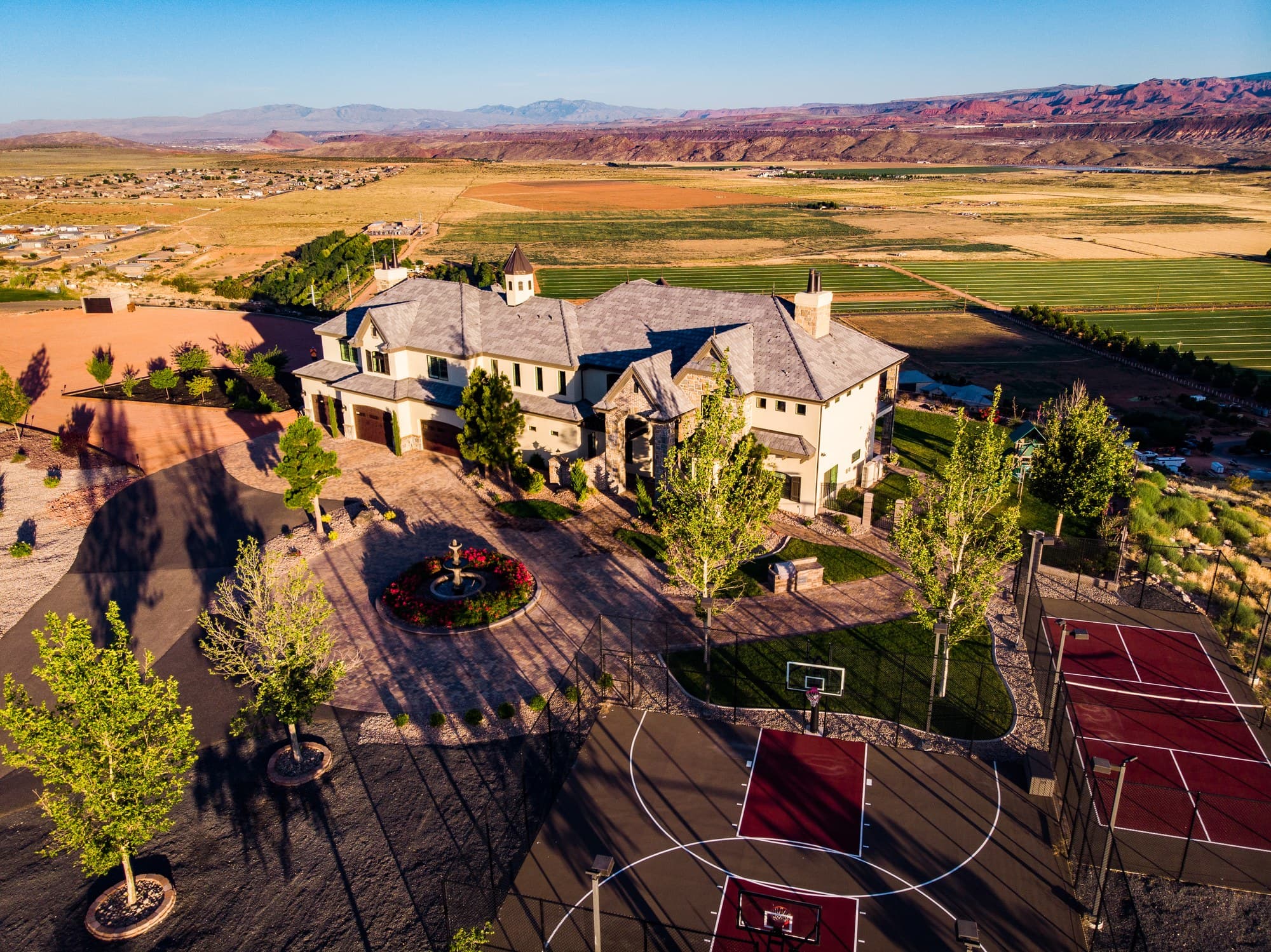 The circular drive and fountain, sport courts in the foreground and the Hurricane fields and red cliffs beyond